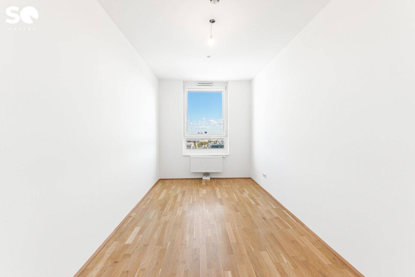 Geräumiges, leeres Zimmer mit Parkettboden und einem Fenster mit Blick nach draußen.