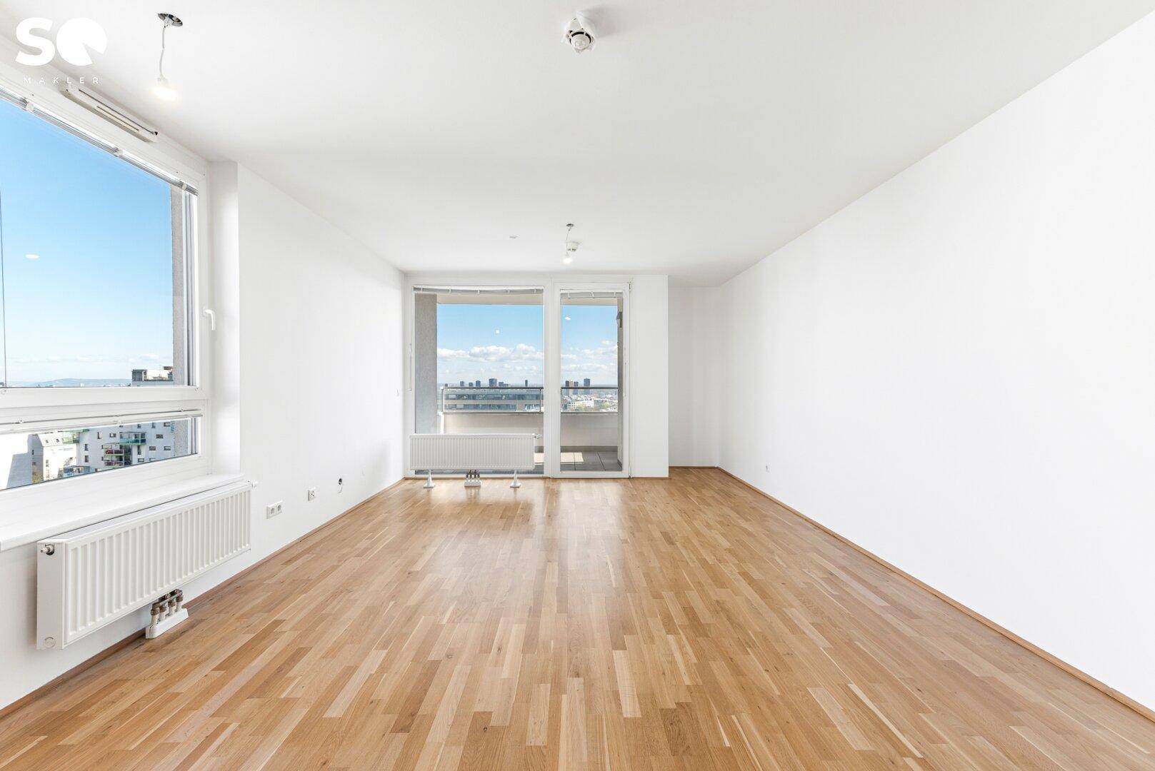 Helles, leeres Wohnzimmer mit Parkettboden und großen Fenstern, die viel Tageslicht hereinlassen.