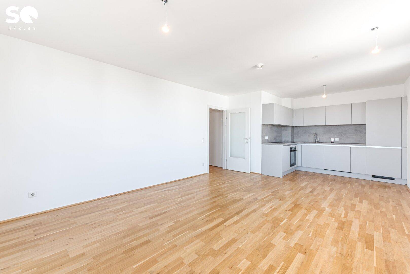 Heller Wohnbereich mit integrierter, minimalistischer Küche und Zugang zu weiteren Räumen.