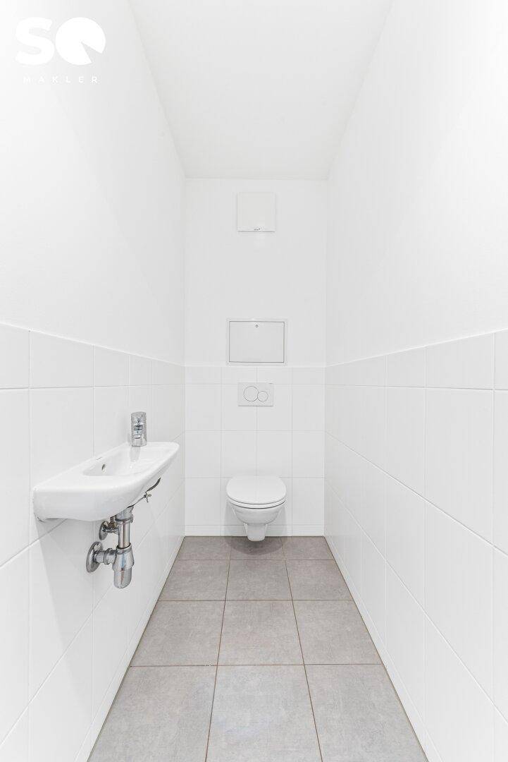 Separates Gäste-WC mit wandhängender Toilette und kleinem Waschbecken, modern gefliest.