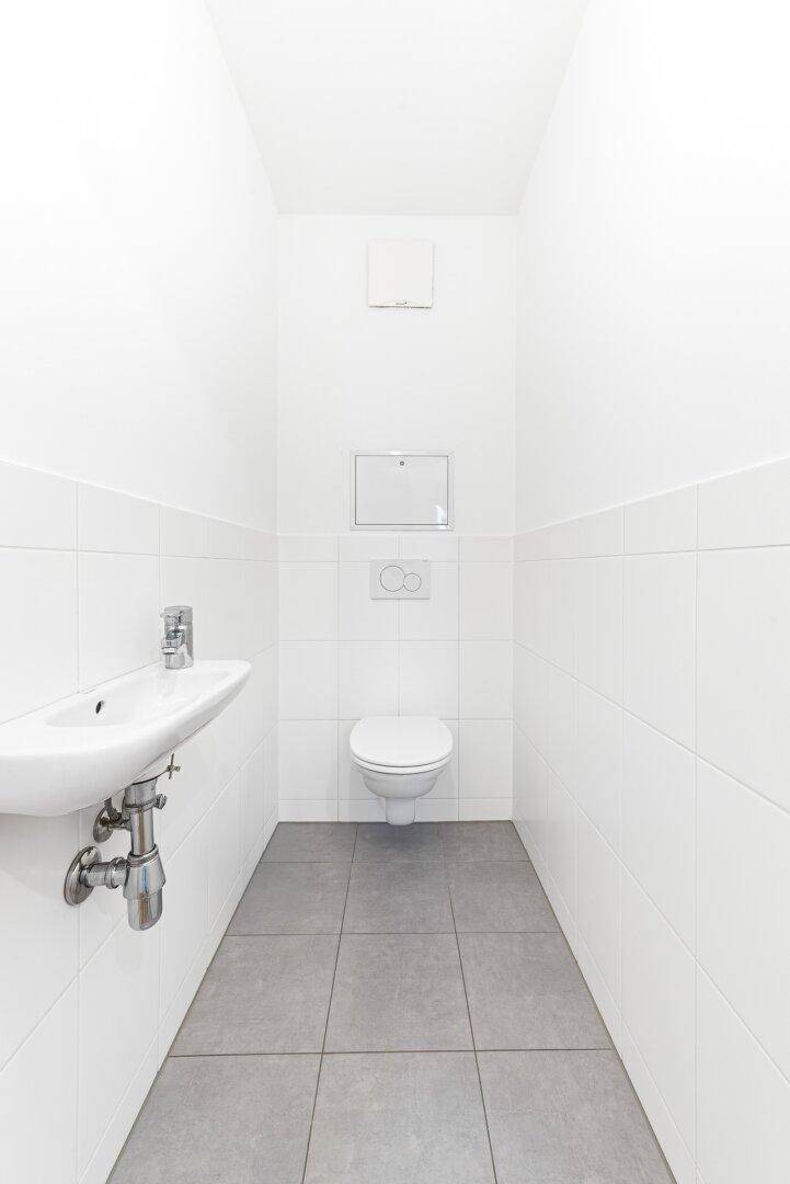 Kleines, hell gefliestes Gäste-WC mit wandhängendem WC und Handwaschbecken.