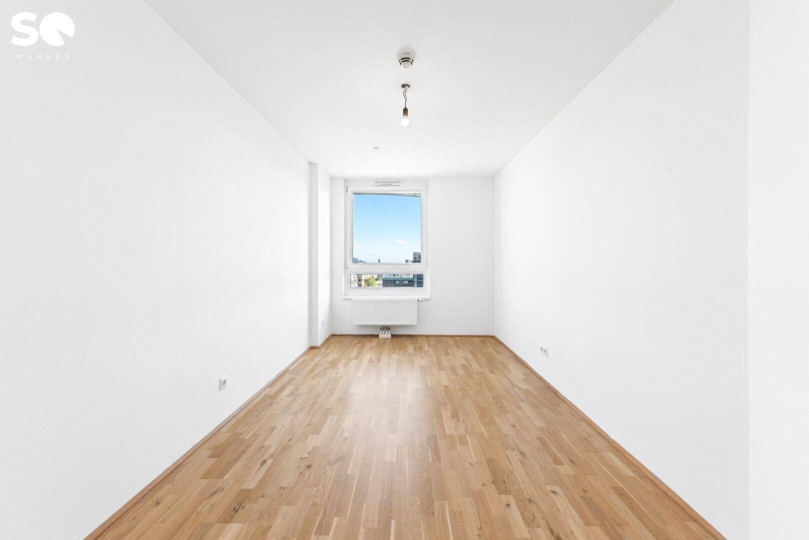 Langes, helles Zimmer mit Parkettboden und einem Fenster, das einen weiten Blick bietet.