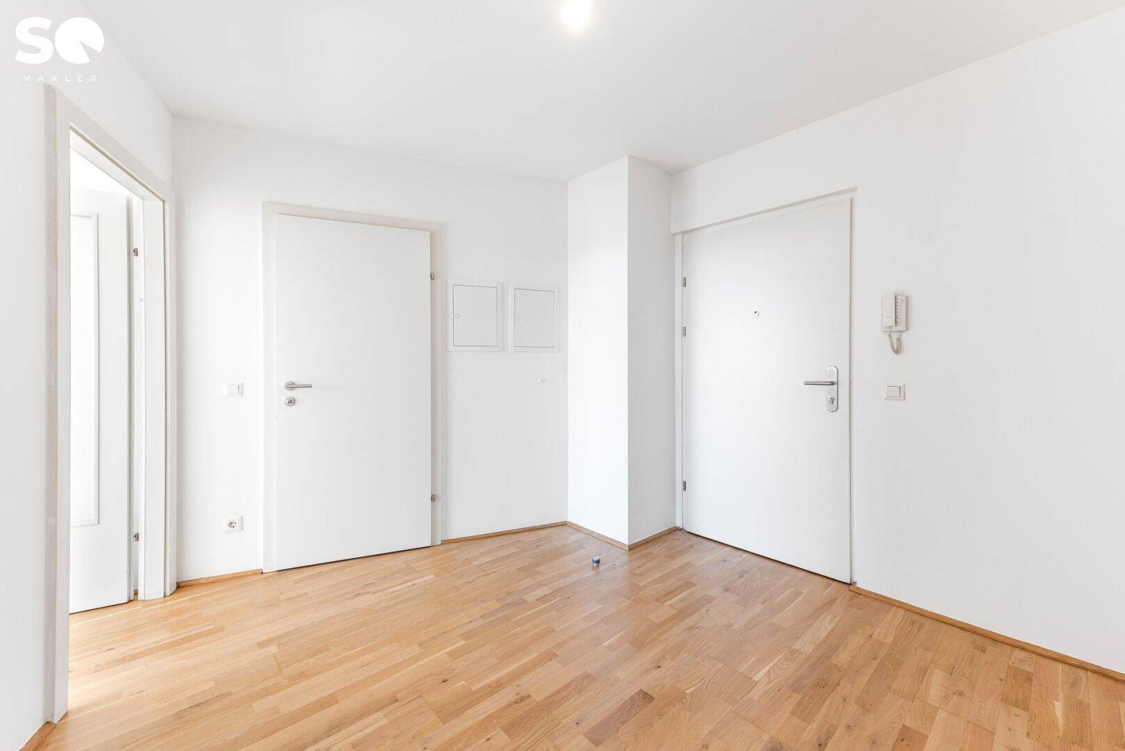 Eingangsbereich mit Parkettboden, weißen Türen und einer Gegensprechanlage an der Wand.