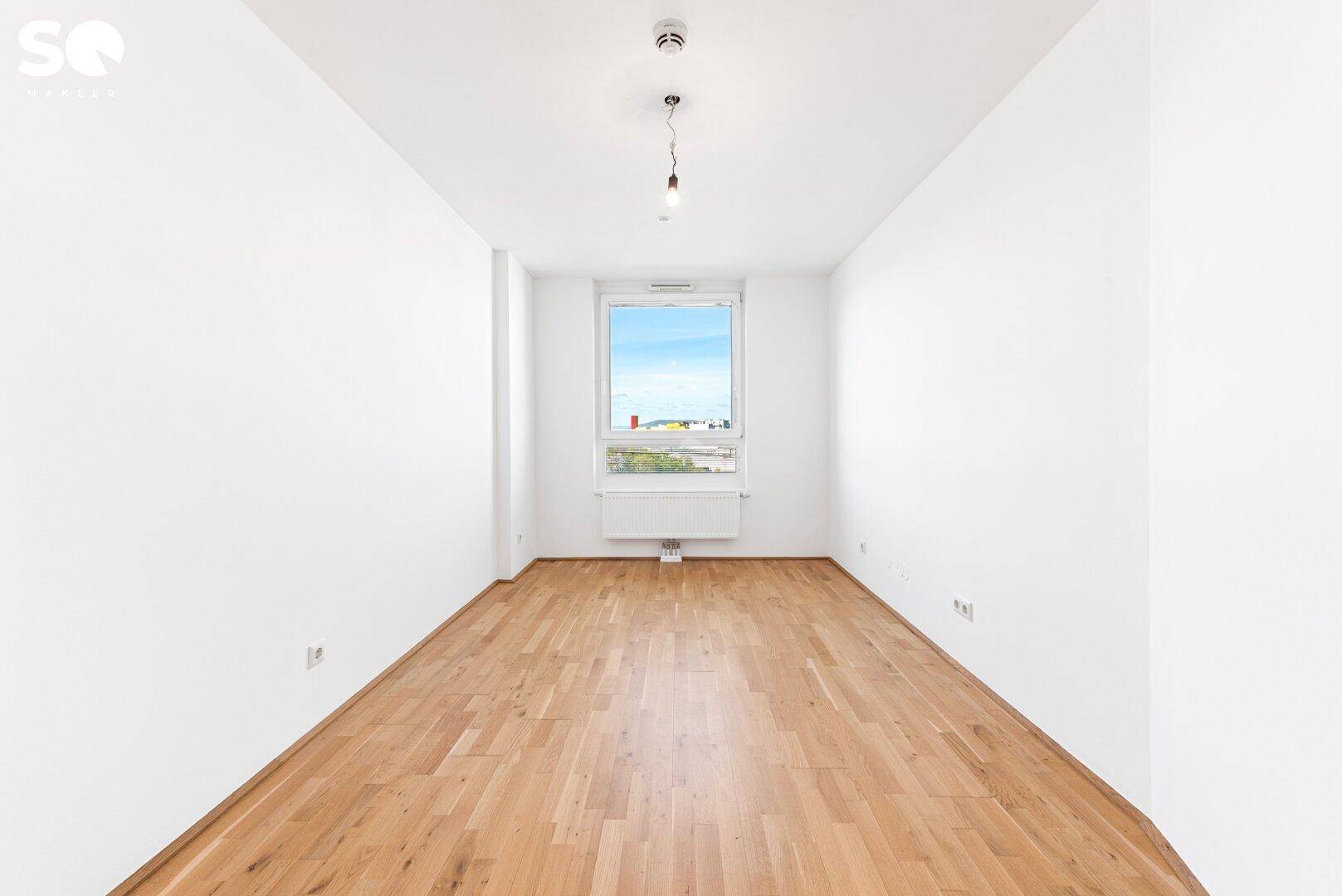 Helles Schlafzimmer mit Parkettboden und einem großen Fenster, bietet eine ruhige Atmosphäre.
