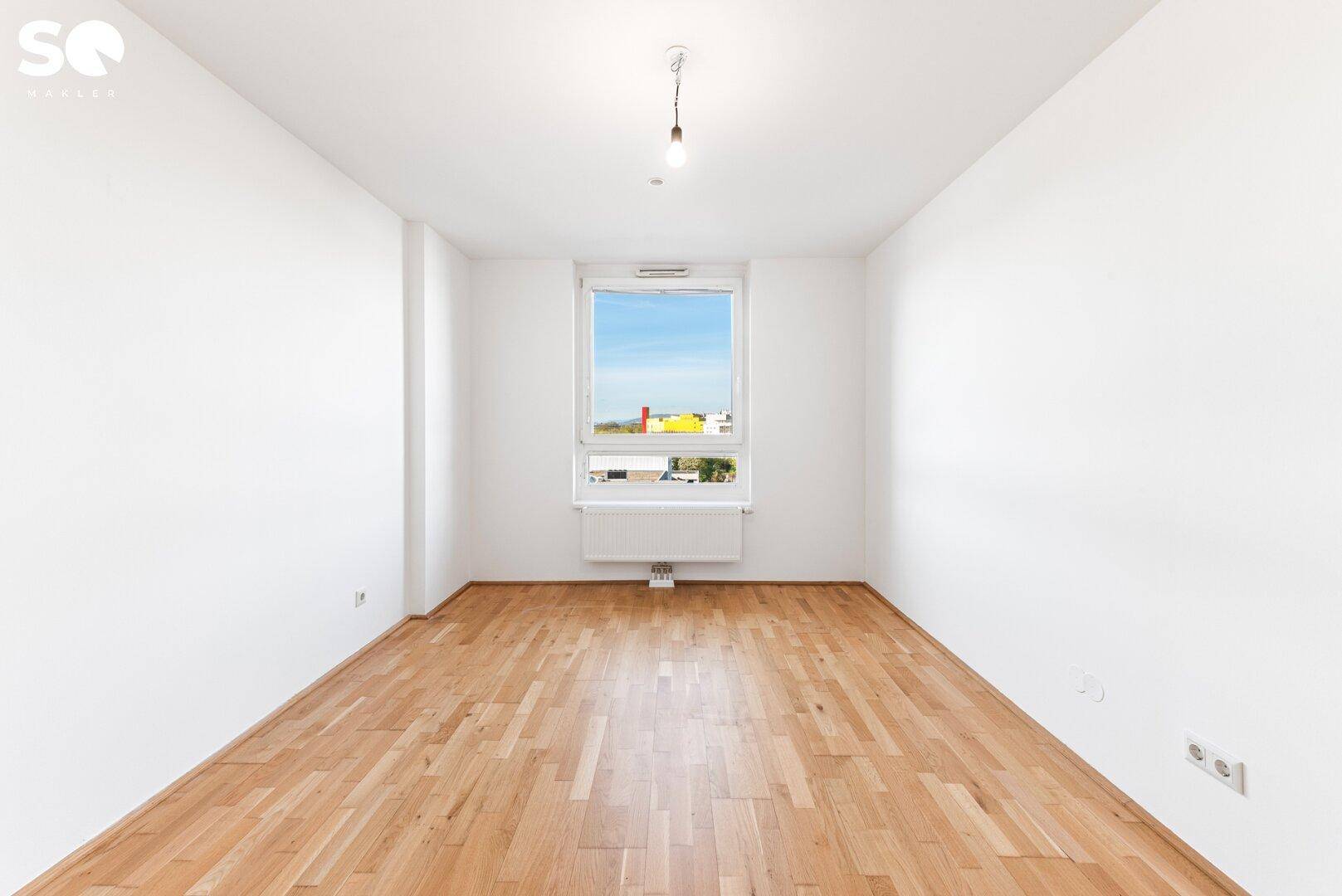 Helles Schlafzimmer mit Parkettboden und großem Fenster, ideal für natürliche Belichtung.