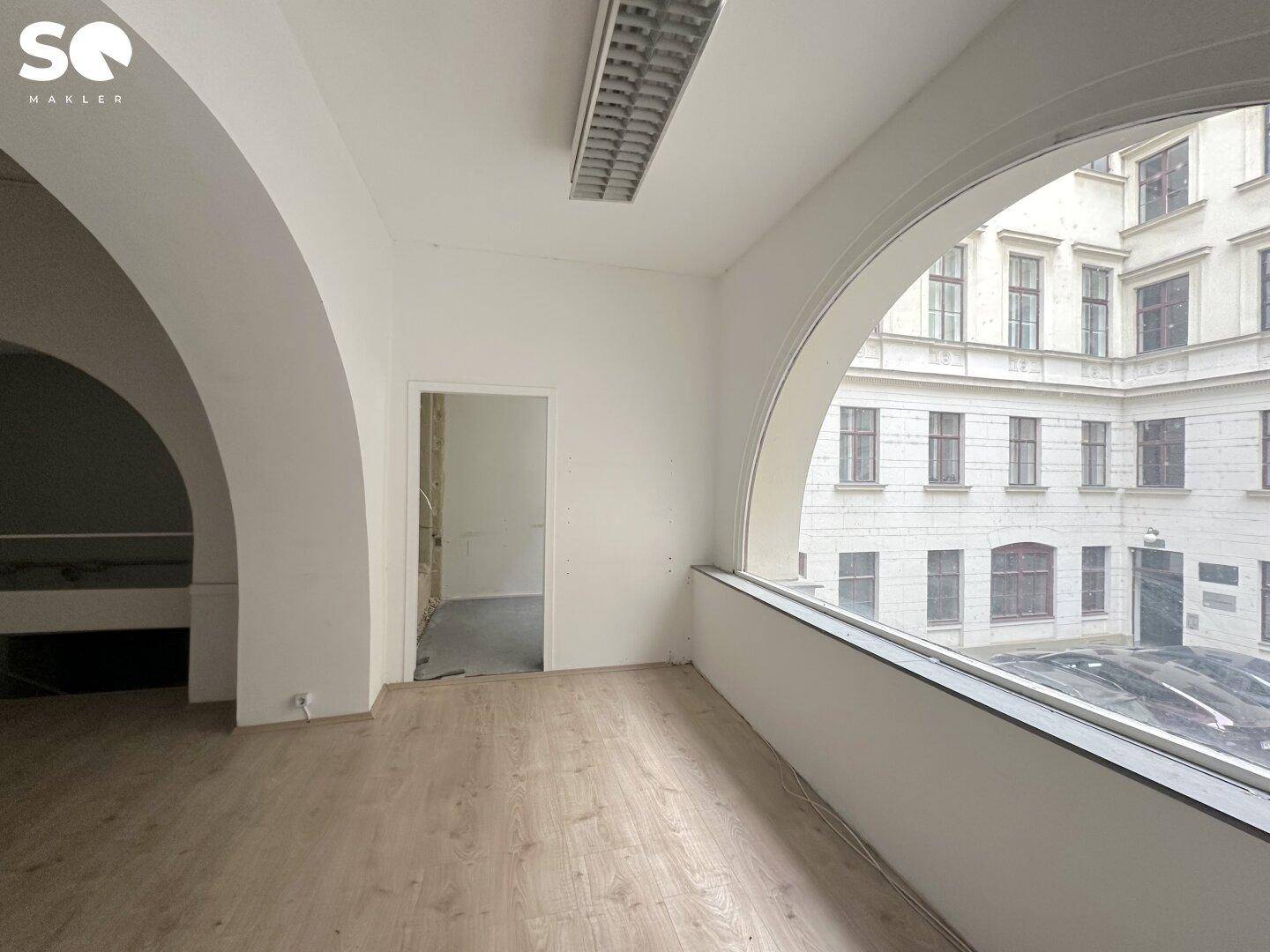Heller Raum mit Holzboden, gewölbten Durchgängen und Blick auf einen ruhigen Innenhof.