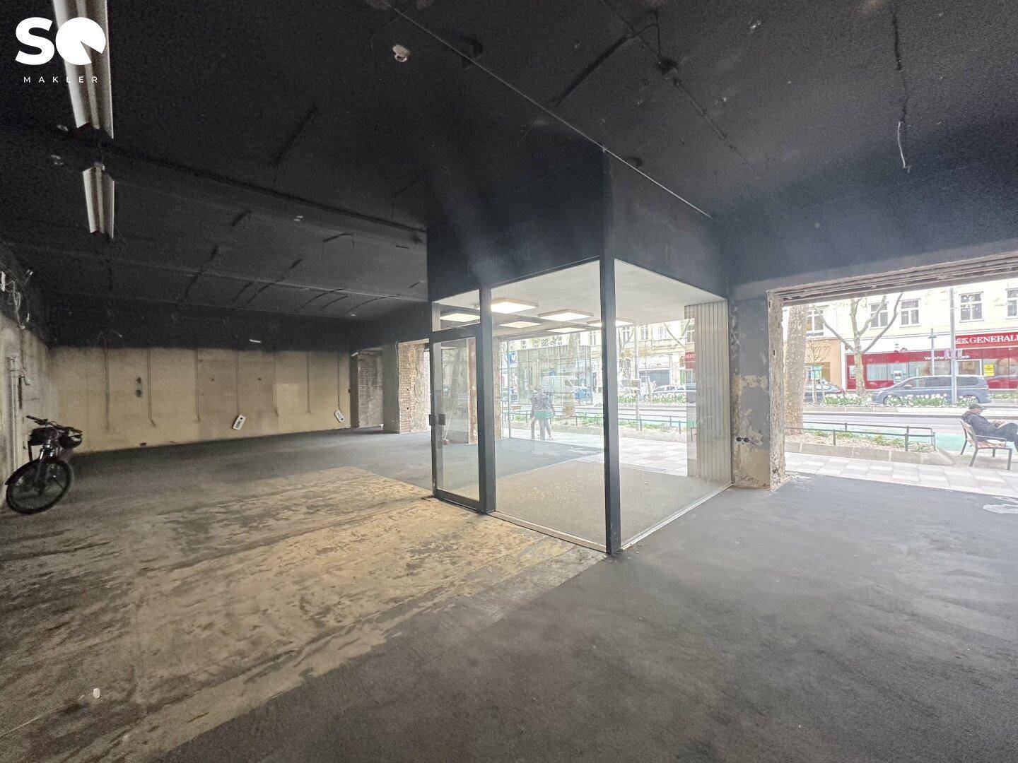 Großer, leerer Geschäftsraum mit dunklem Boden und Decke, bereit für den Ausbau und mit viel Tageslicht.