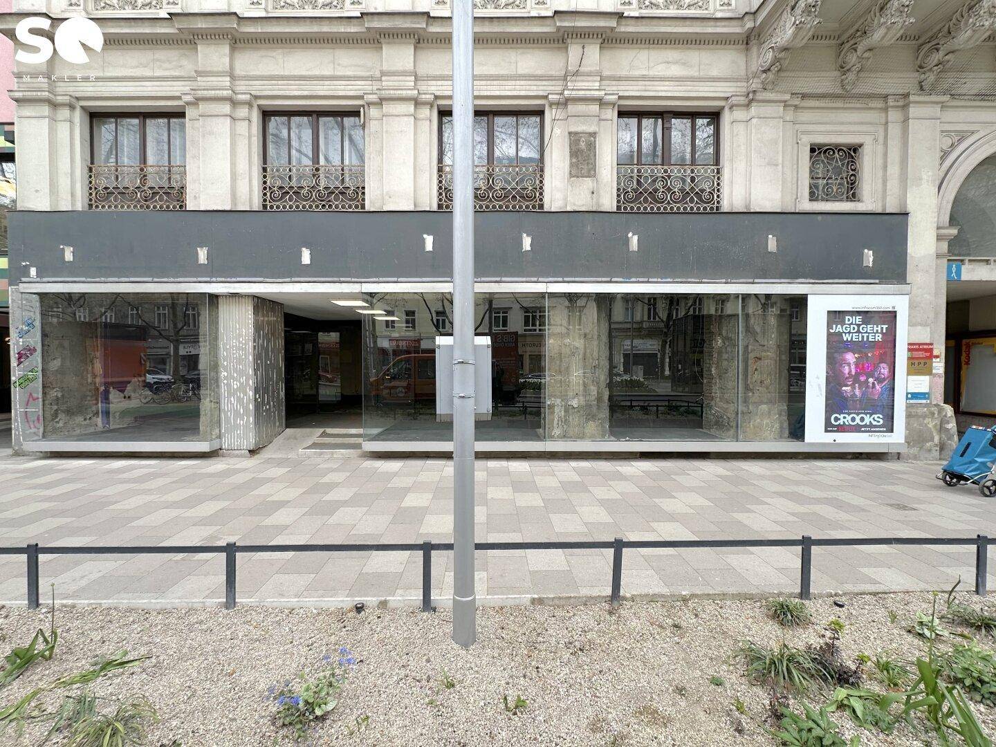 Frontansicht eines Geschäftsgebäudes mit breiter Glasfront und einem Werbeplakat an der Seite des Eingangs.