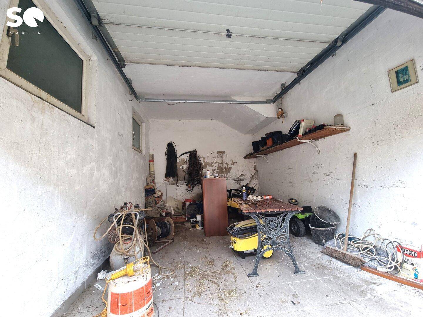 Innenansicht einer Garage oder eines Abstellraums mit Betonboden und verschiedenen Gegenständen.