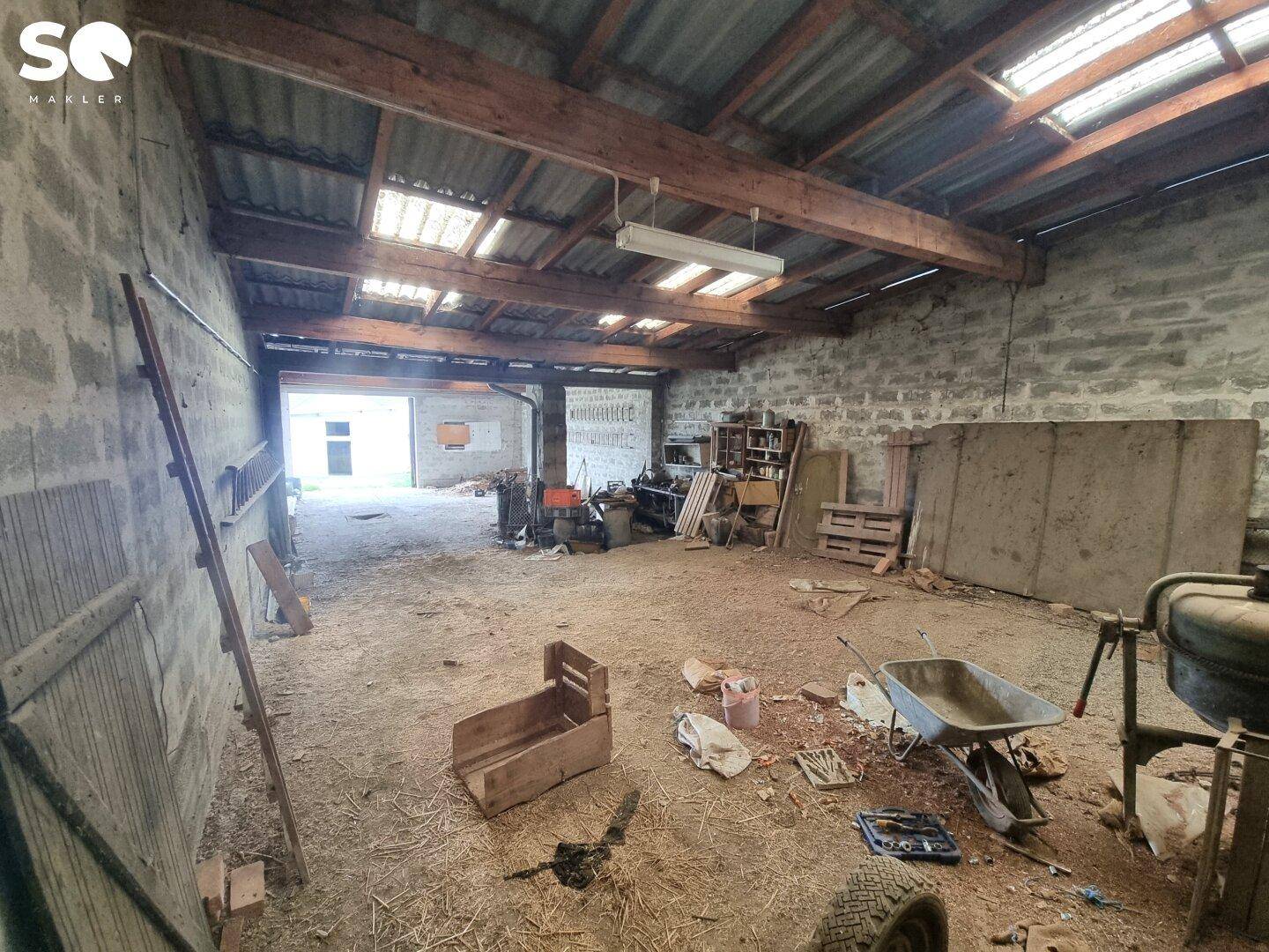 Geräumige Scheune mit Holzdachkonstruktion, Ziegelwänden und verschiedenen landwirtschaftlichen Geräten.