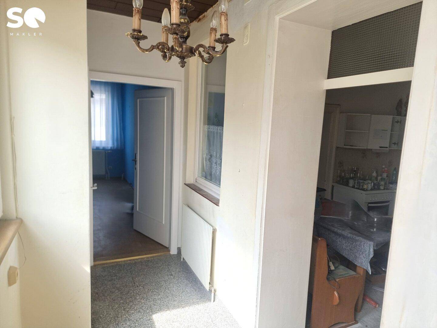 Flur mit Terrazzoboden, einem Fenster und einem traditionellen Kronleuchter, der den Raum erhellt.