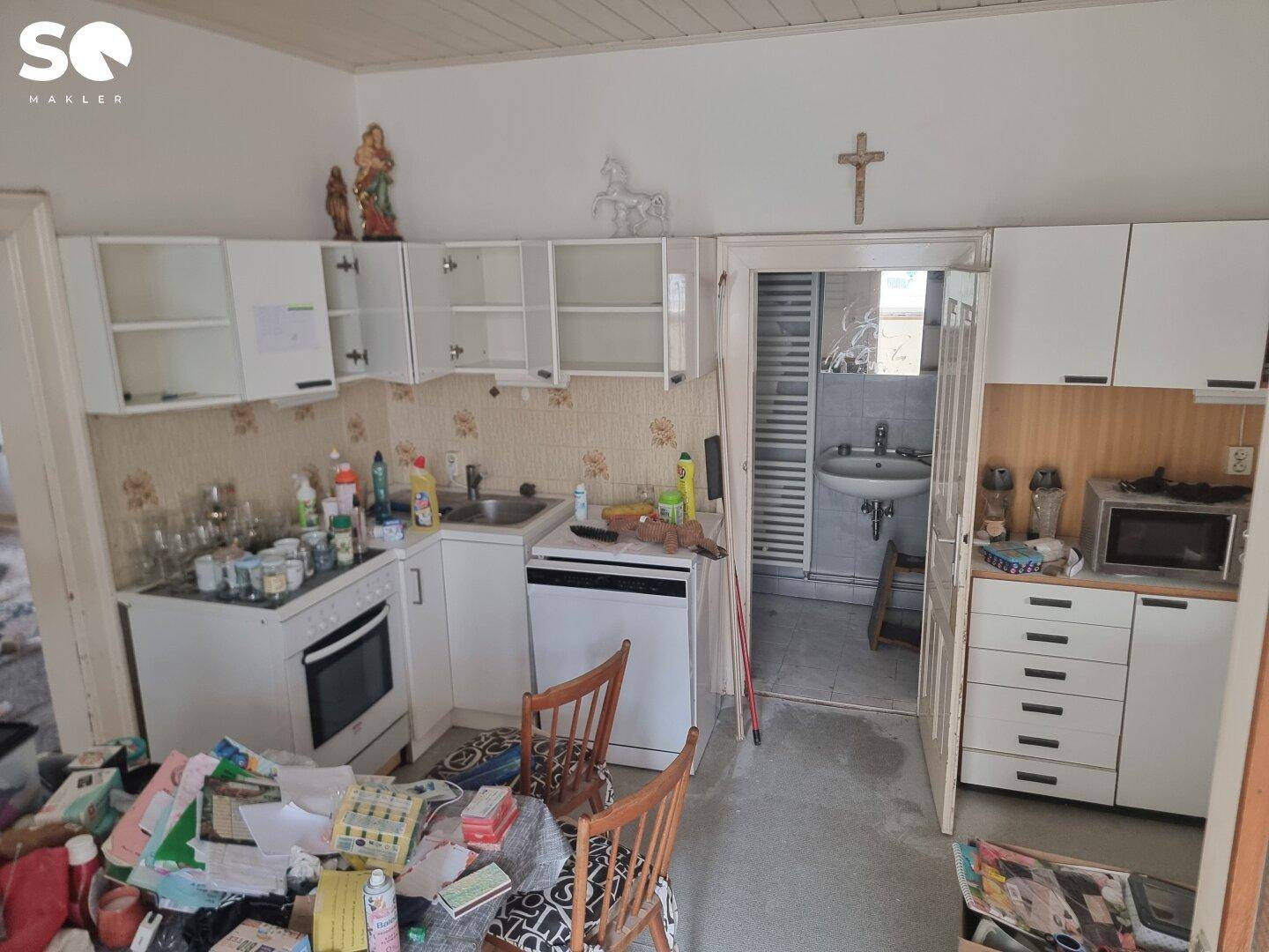 Einfache Küche mit weißen Schränken, Spüle und Blick in ein angrenzendes Badezimmer.