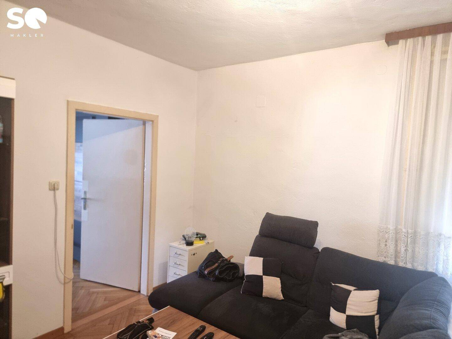 Detailansicht eines Wohnzimmers mit Sofa und einem Fenster mit weißen Vorhängen, gut beleuchtet.