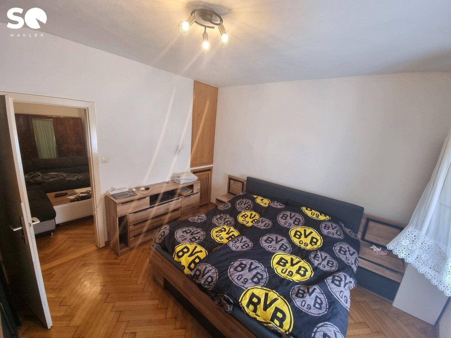 Schlafzimmer mit Parkettboden, Doppelbett und Zugang zu einem angrenzenden Wohnbereich.