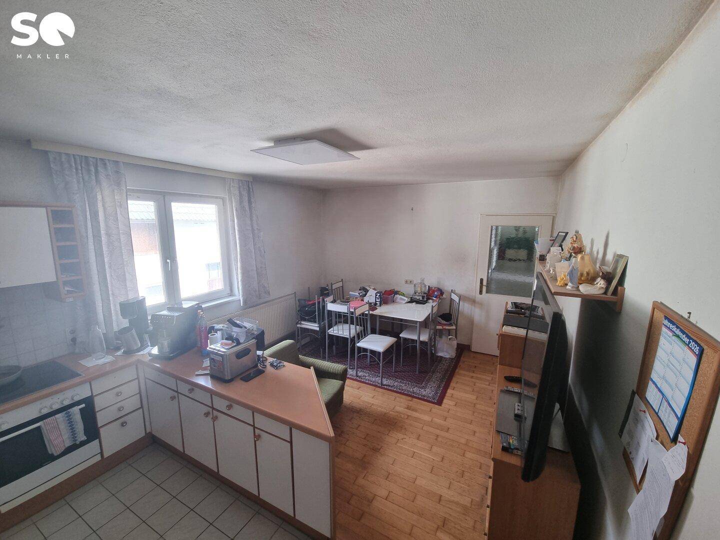 Wohnküche mit Fliesenboden, Einbauküche und einem Essbereich am Fenster, hell und funktional.