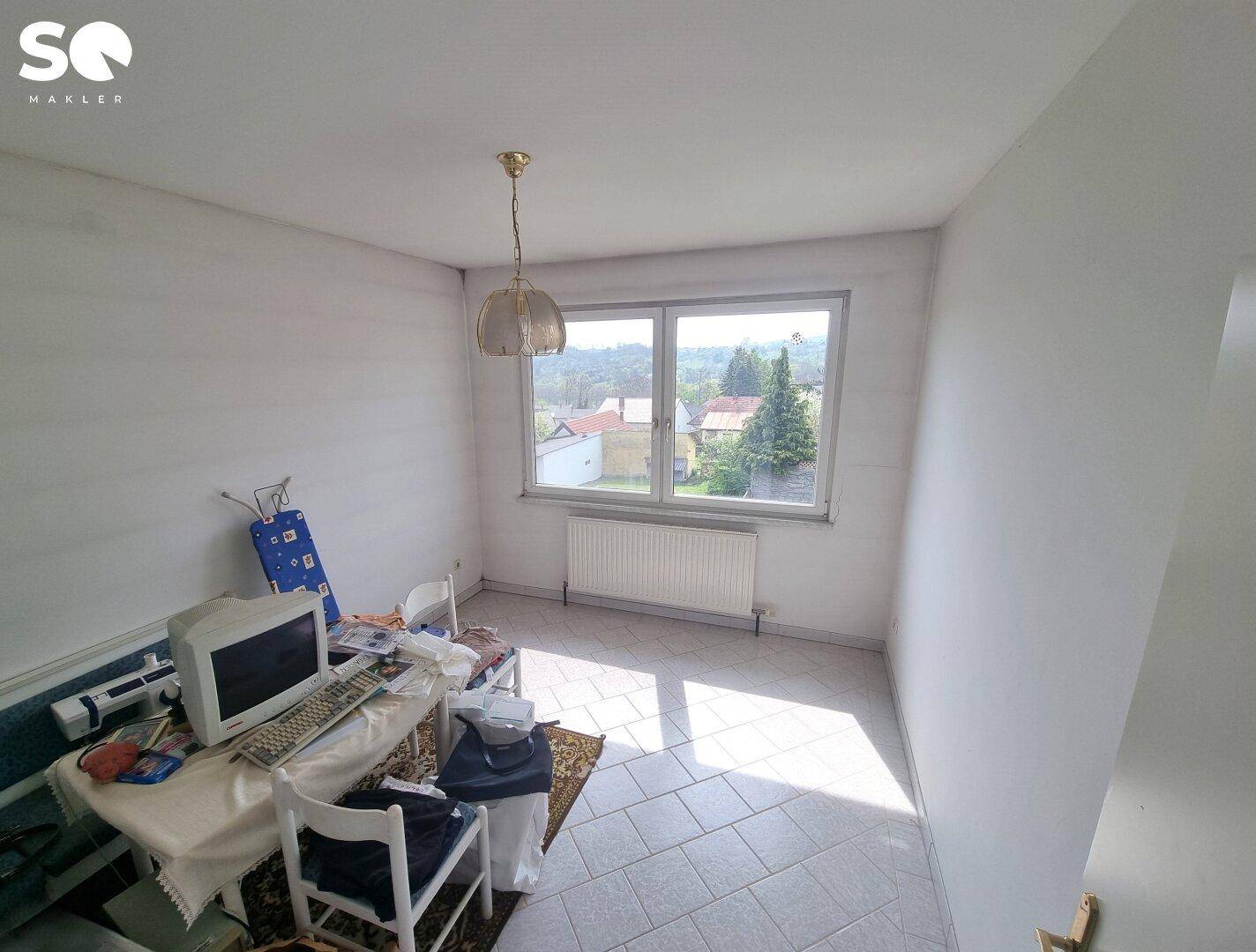 Helles Zimmer mit Fliesenboden, großem Fenster und Blick auf die umliegende Landschaft.