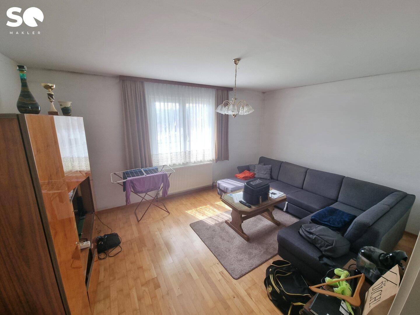 Gemütliches Wohnzimmer mit Parkettboden, Sofa und einem Fenster mit Vorhängen, hell beleuchtet.
