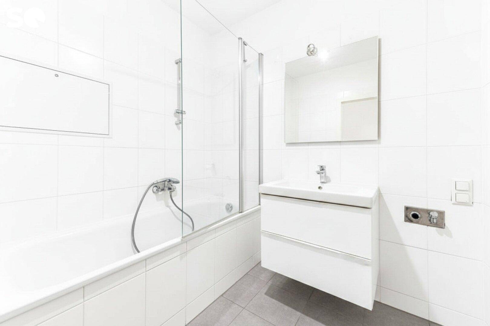 Modernes Badezimmer mit weißen Fliesen, Badewanne und integrierter Duschabtrennung.