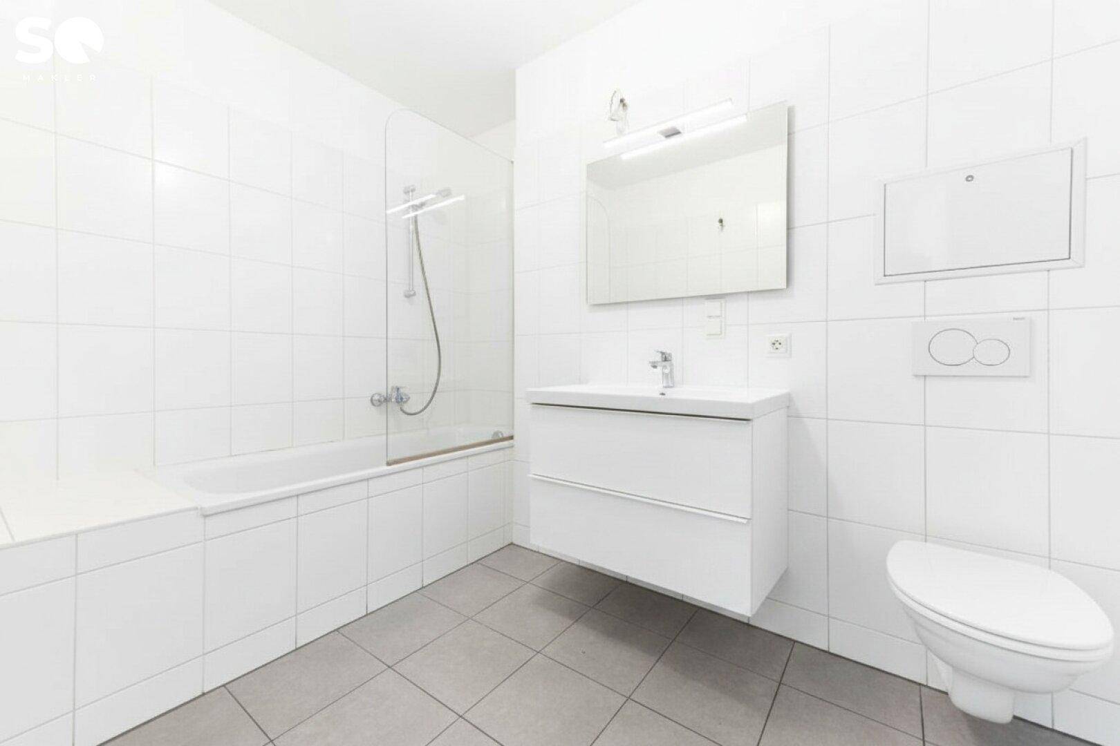 Modernes Badezimmer mit weißen Fliesen, Badewanne mit Duschfunktion und wandhängendem WC.