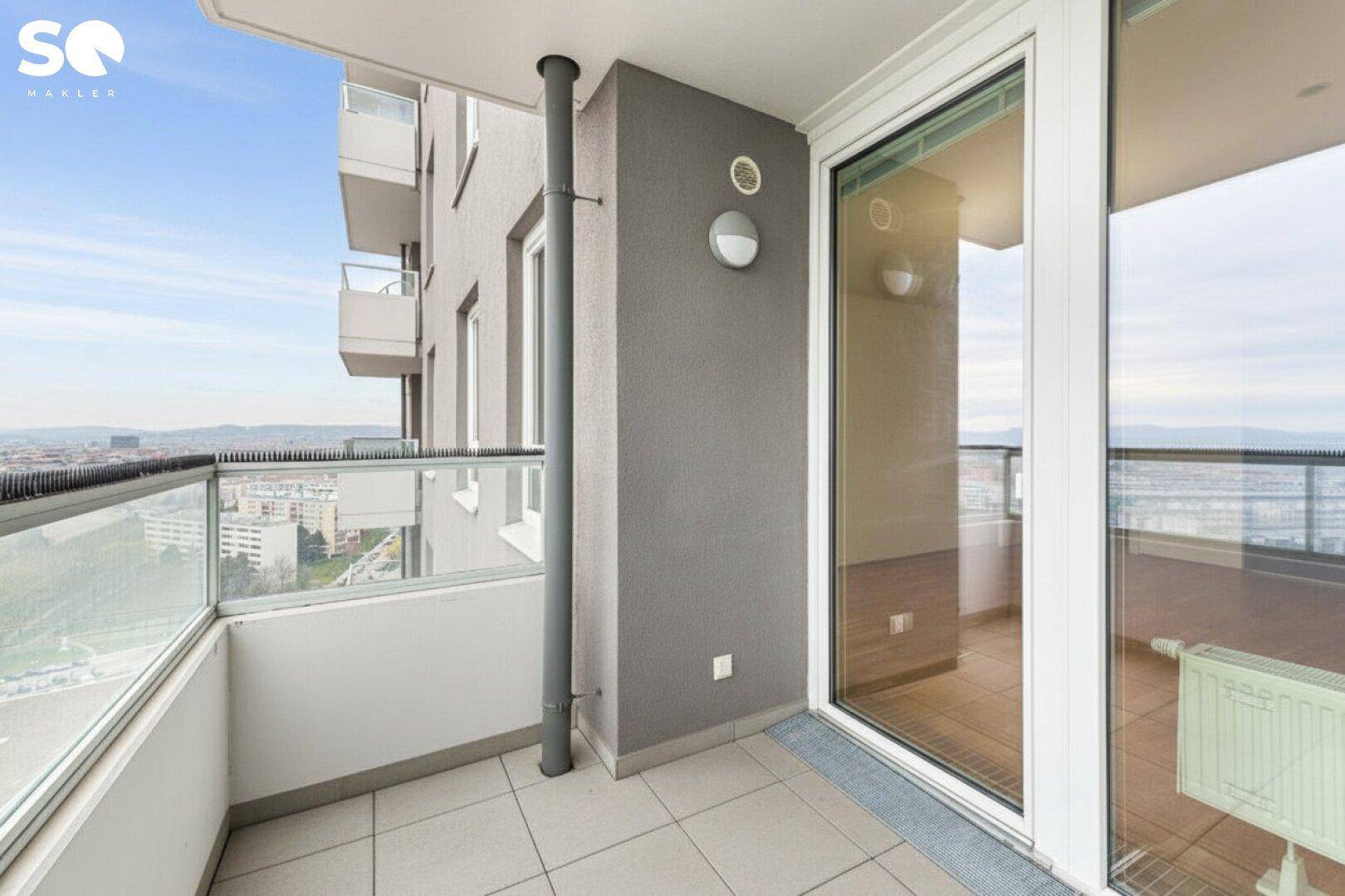 Heller Balkon mit Fliesenboden, Glasgeländer und weitem Blick über die Stadt und Berge.