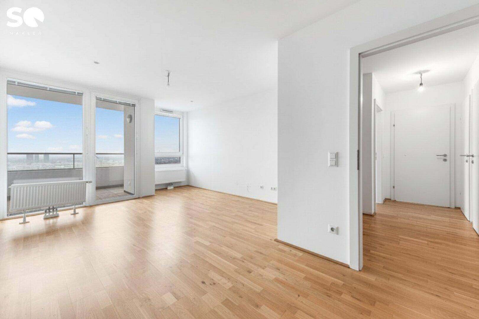 Geräumiges, leeres Wohnzimmer mit Parkettboden, großen Fenstern und Zugang zum Balkon.