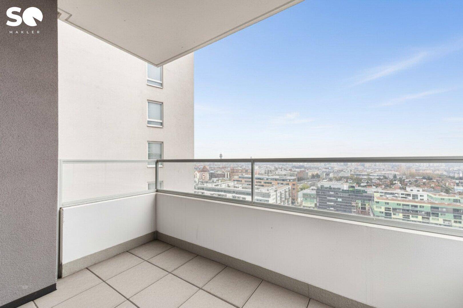Geräumiger Balkon mit Fliesenboden und Glasgeländer, bietet einen weiten Blick über die Stadt.