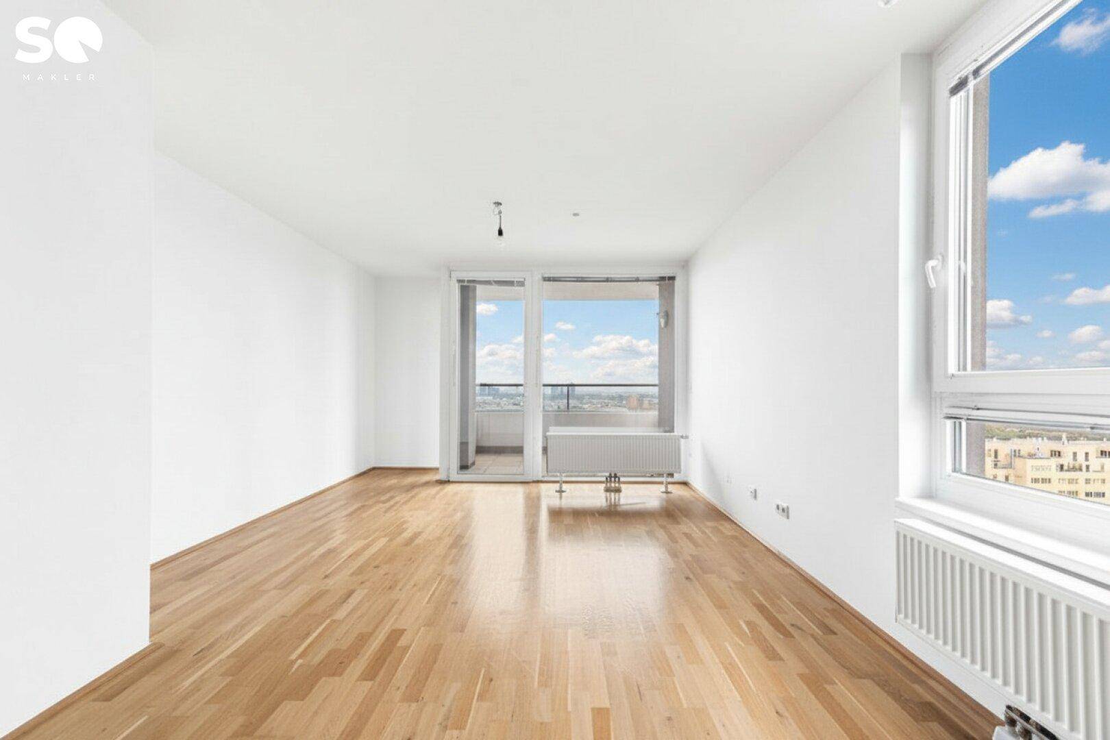 Heller, leerer Raum mit Holzboden und großen Fenstern, die Zugang zu einem Balkon bieten.