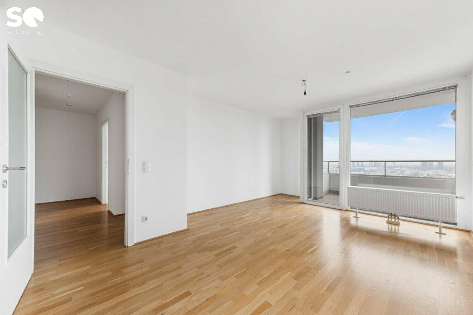 Geräumiger, heller Wohnbereich mit Holzboden und Zugang zu einem Balkon mit Stadtblick.