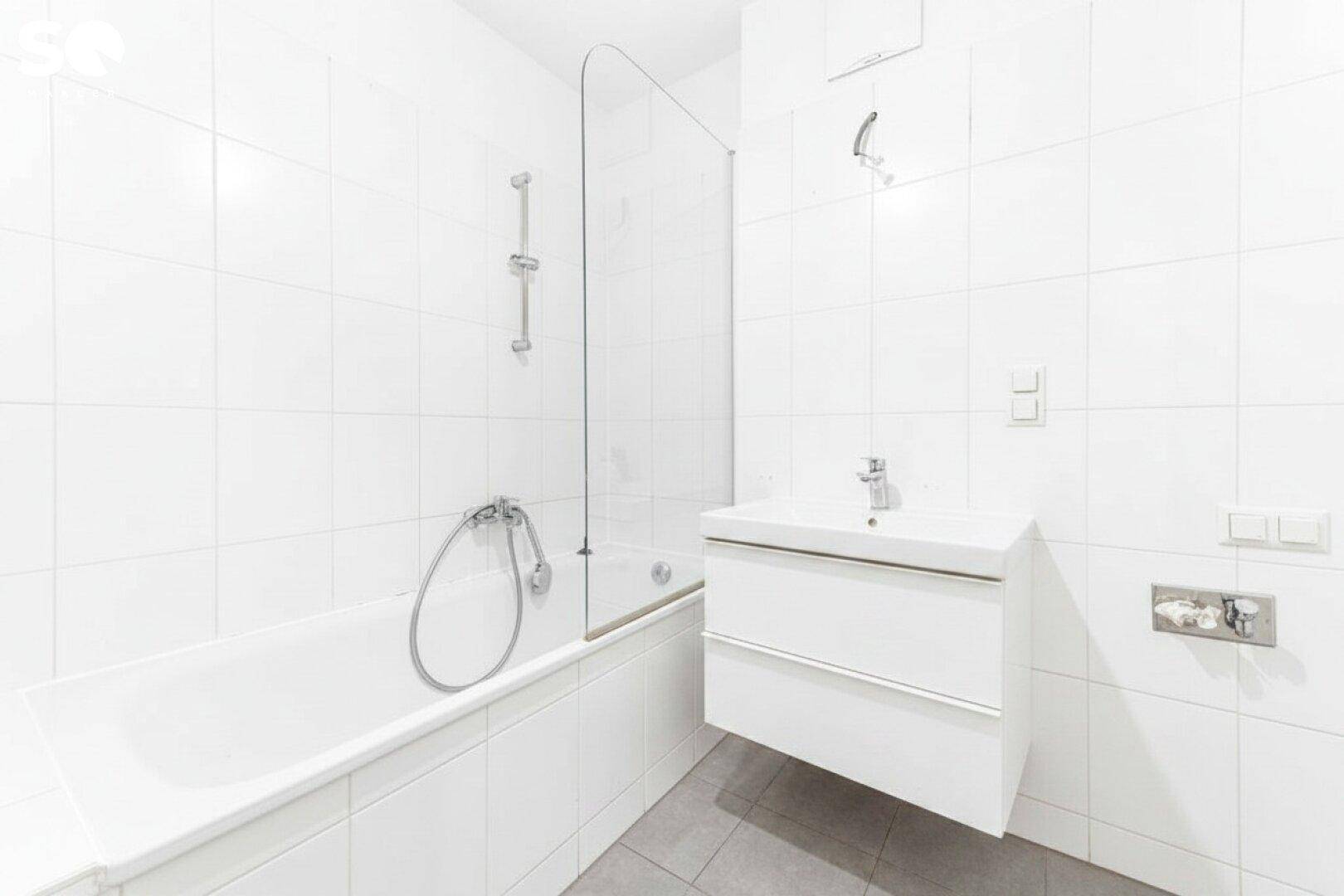 Modernes Badezimmer mit weißen Fliesen, Badewanne mit Duschwand und einem Waschbecken.