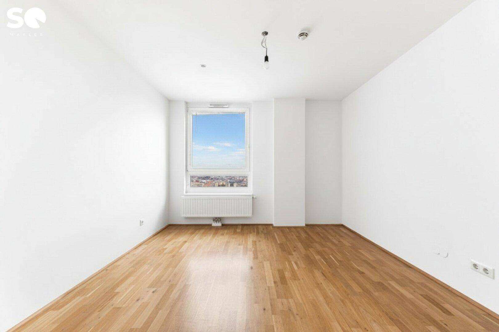Leeres Schlafzimmer mit Holzboden und einem Fenster, das einen weiten Blick auf die Stadt bietet.