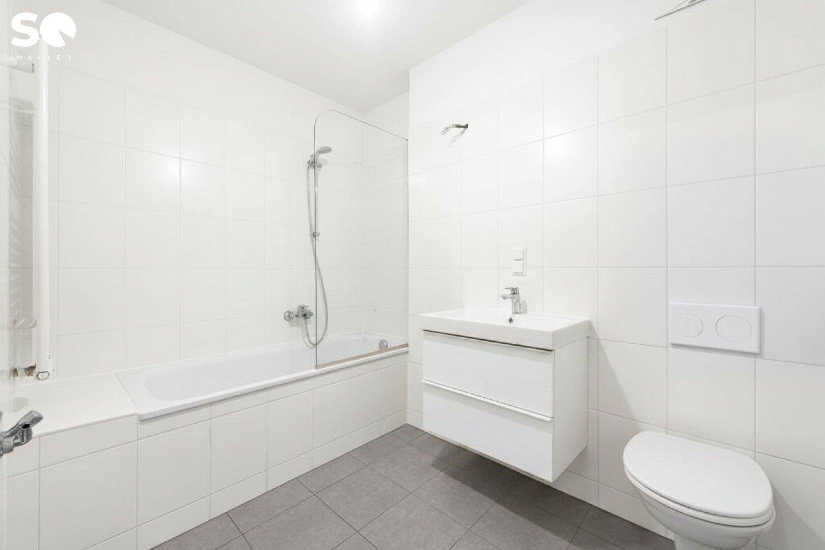 Modernes Badezimmer mit weißen Fliesen, Badewanne mit Duschwand und wandhängendem WC.