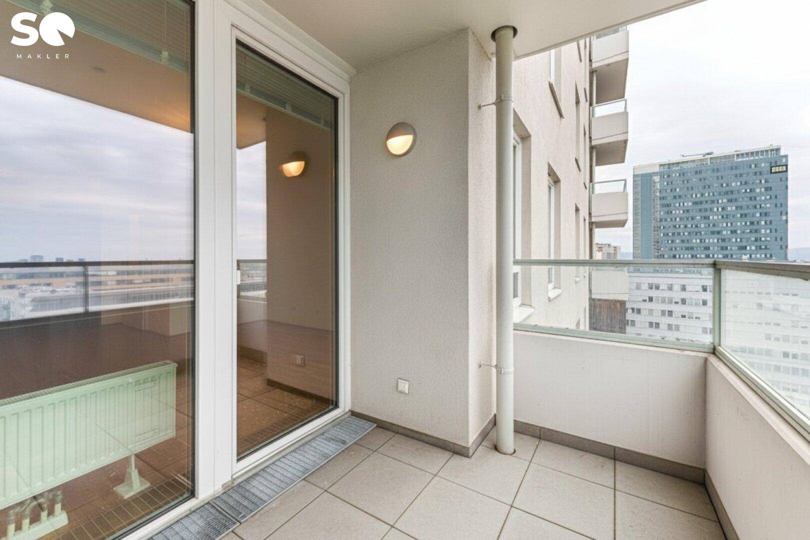 Heller Balkon mit Fliesenboden und Glasbrüstung, bietet einen weiten Blick über die Stadt.