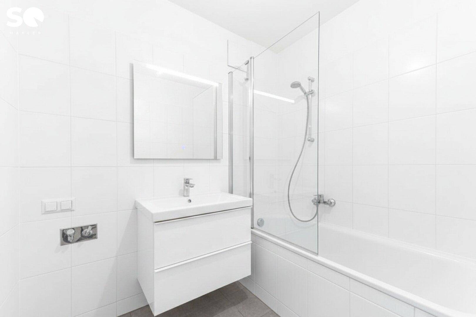Modernes Badezimmer mit Badewanne, Duschwand und weiß gefliesten Wänden.