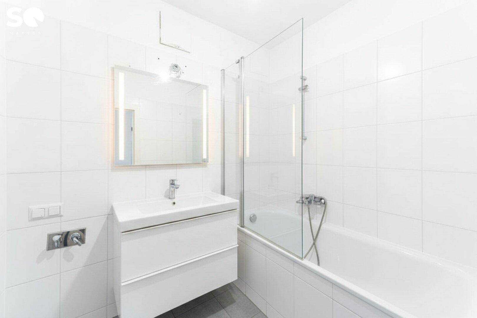 Modernes Badezimmer mit Badewanne, Duschabtrennung, weißem Waschtisch und Fliesen.