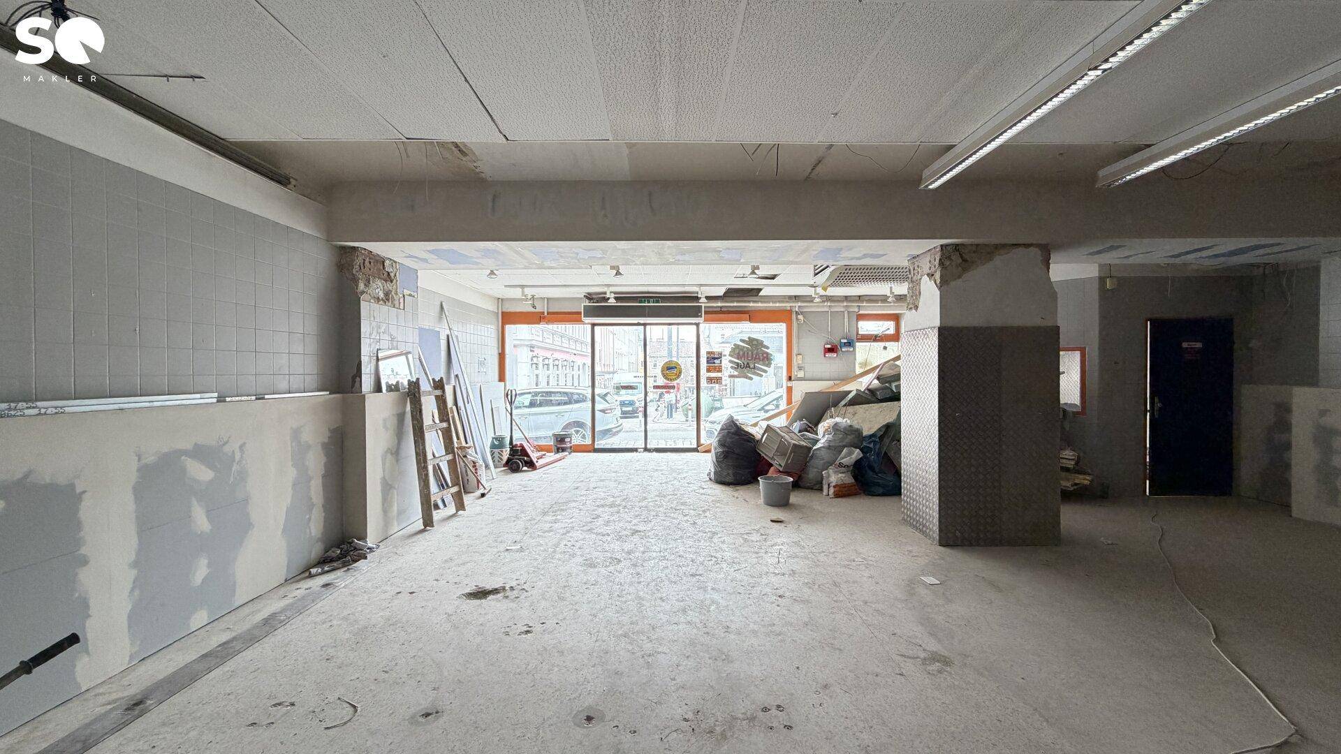 Leerstehender Gewerberaum im Erdgeschoss mit Blick auf die Straße und Fliesen an den Wänden.