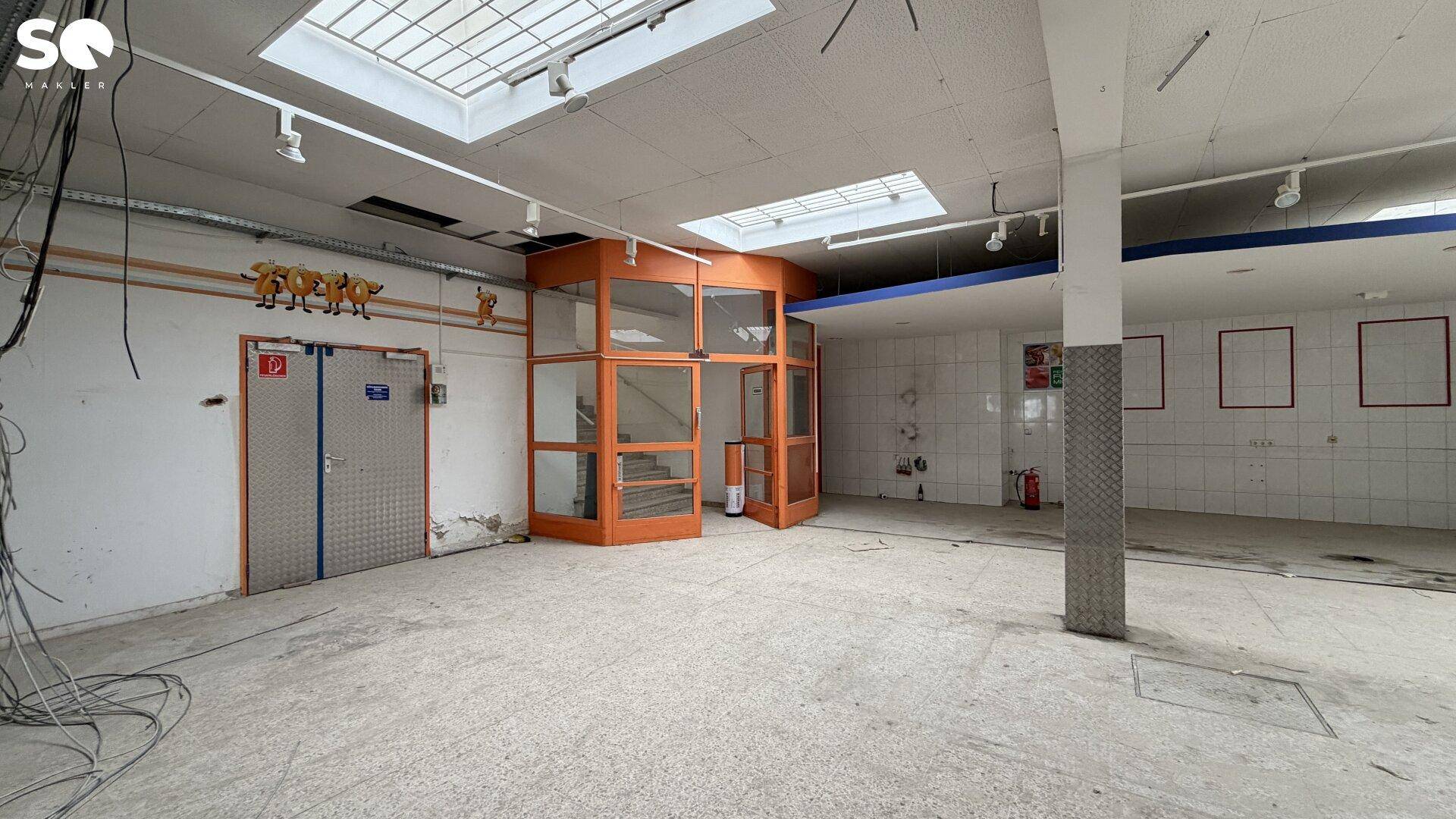 Großer Gewerberaum mit Oberlichtern, Fliesenwänden und einer markanten orangefarbenen Glasstruktur.