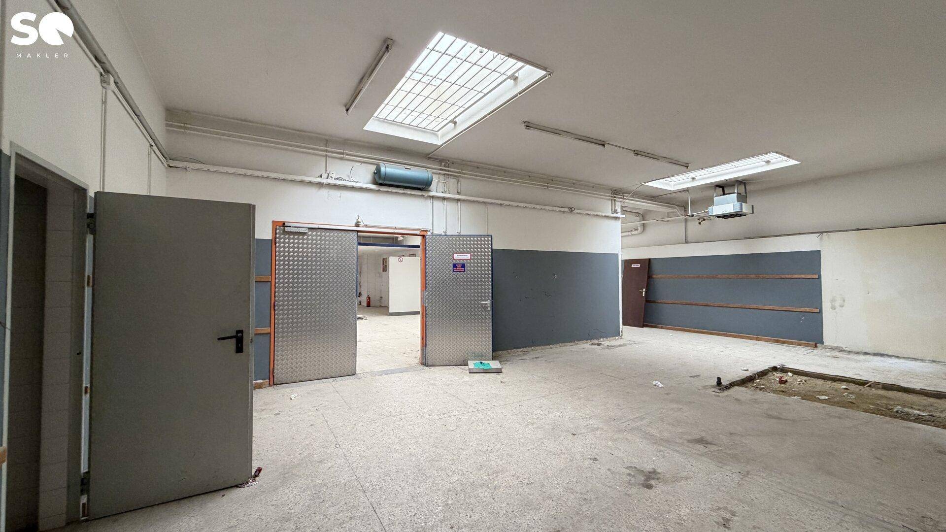 Geräumiger Gewerberaum mit Oberlichtern, grauen Wänden und mehreren Metalltüren, bereit für den Umbau.