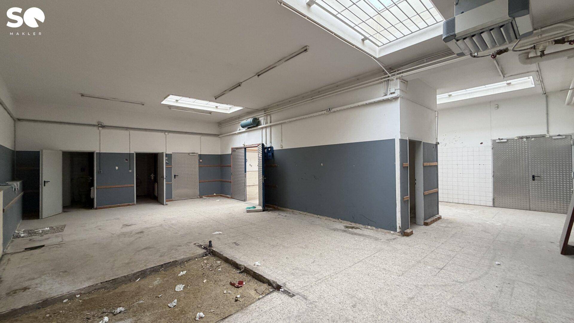Großer Gewerberaum mit Oberlichtern, grauen Wänden und gefliesten Bereichen, bereit für die Neugestaltung.