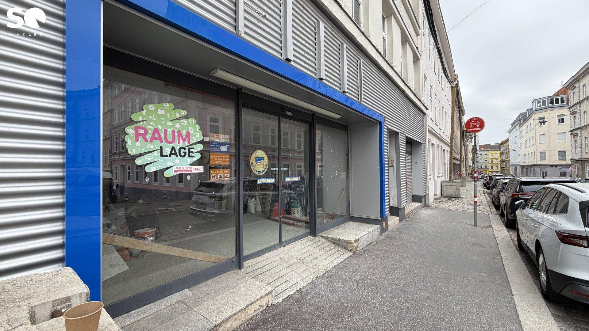 Außenansicht eines Geschäftsgebäudes mit großen Schaufenstern und blauer Fassadenverkleidung an der Straße.
