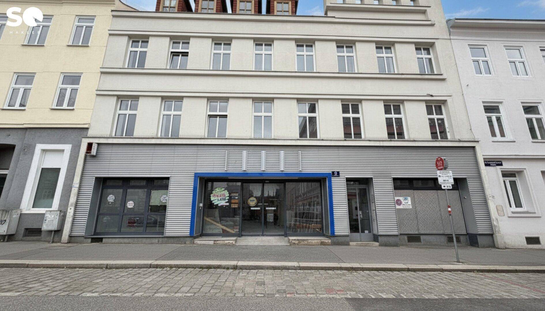 Fassade eines mehrstöckigen Gebäudes mit Geschäftsräumen im Erdgeschoss und Wohnungen darüber.