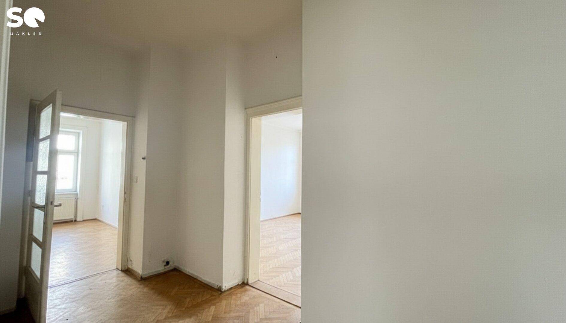 Heller Flur mit Fischgrätparkett und Türen zu angrenzenden, leeren Räumen.