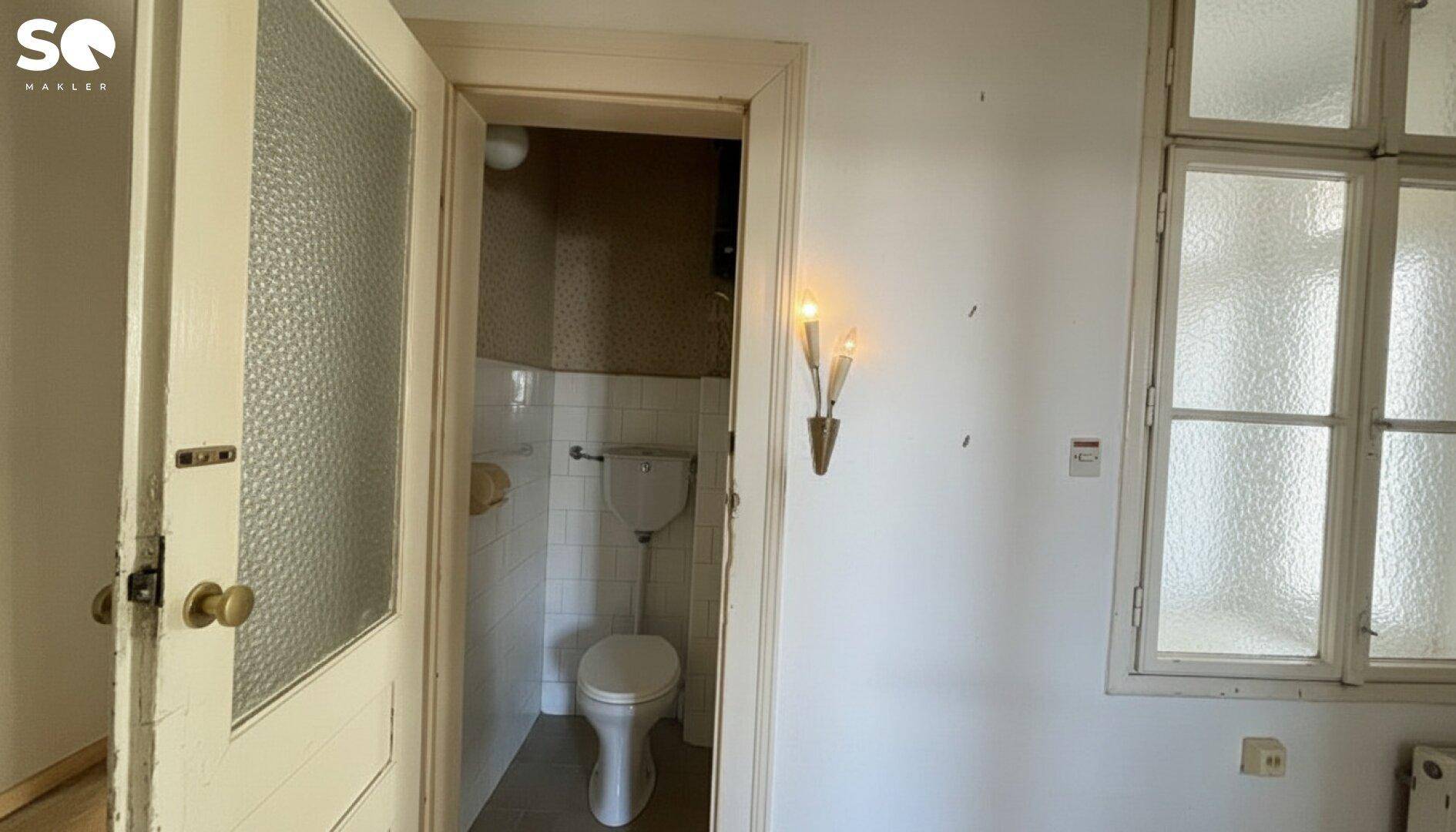 Kleines WC mit Fenster und einfacher Ausstattung, das eine Modernisierung benötigt.