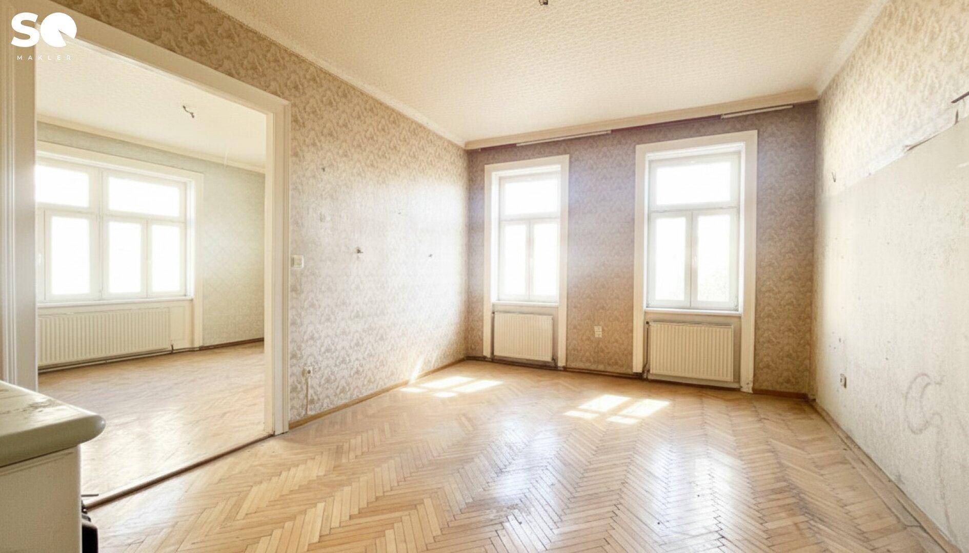 Helles Zimmer mit Fischgrätparkett und zwei großen Fenstern, bereit zur Renovierung.