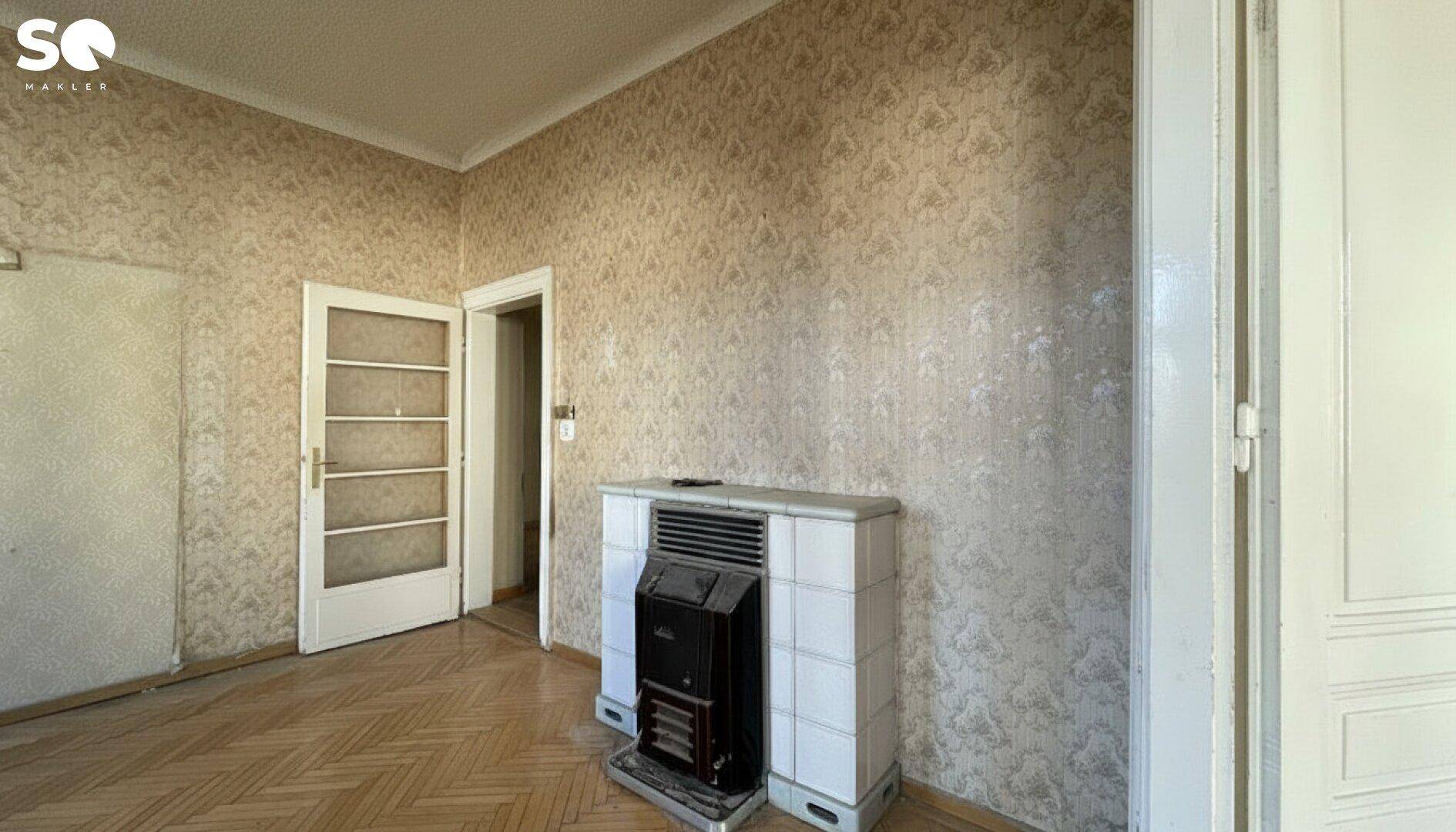 Geräumiges Zimmer mit Fischgrätparkett und einem traditionellen Ofen, der auf Renovierung wartet.