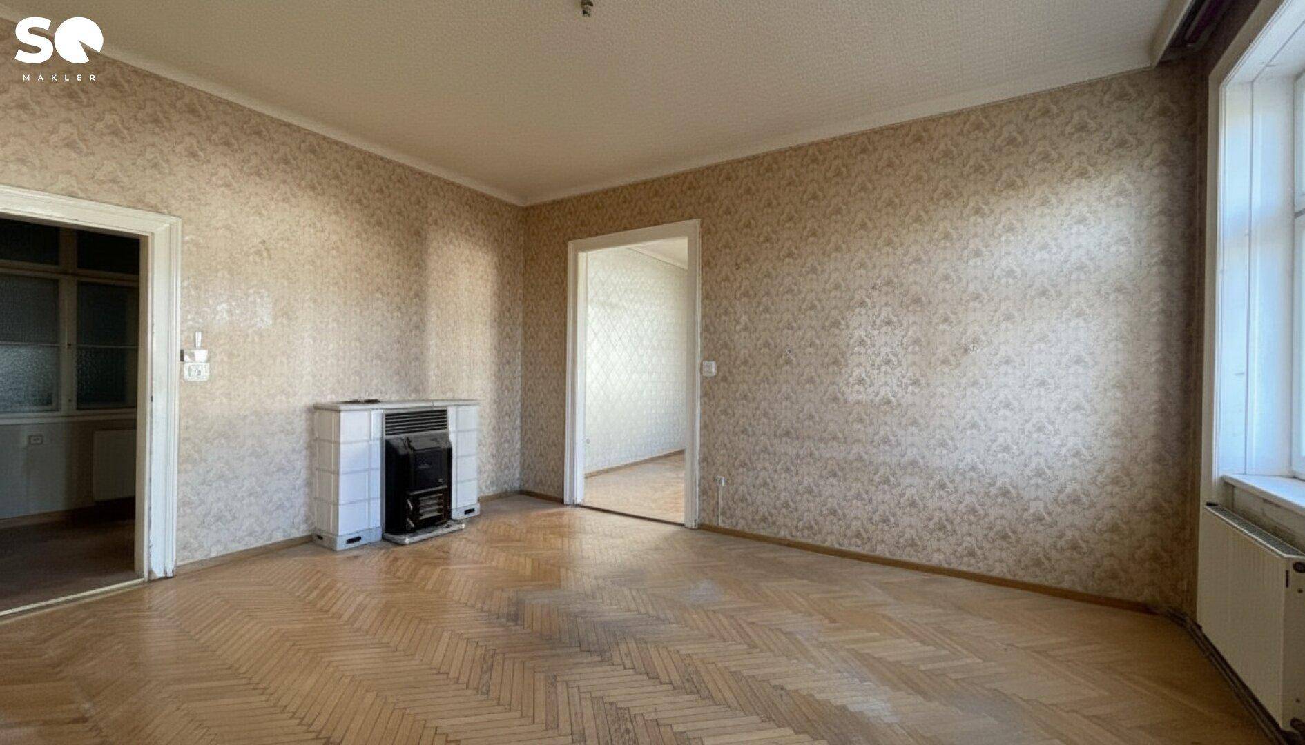 Großes Zimmer mit Fischgrätparkett und zwei Türen, die zu weiteren Räumen führen.
