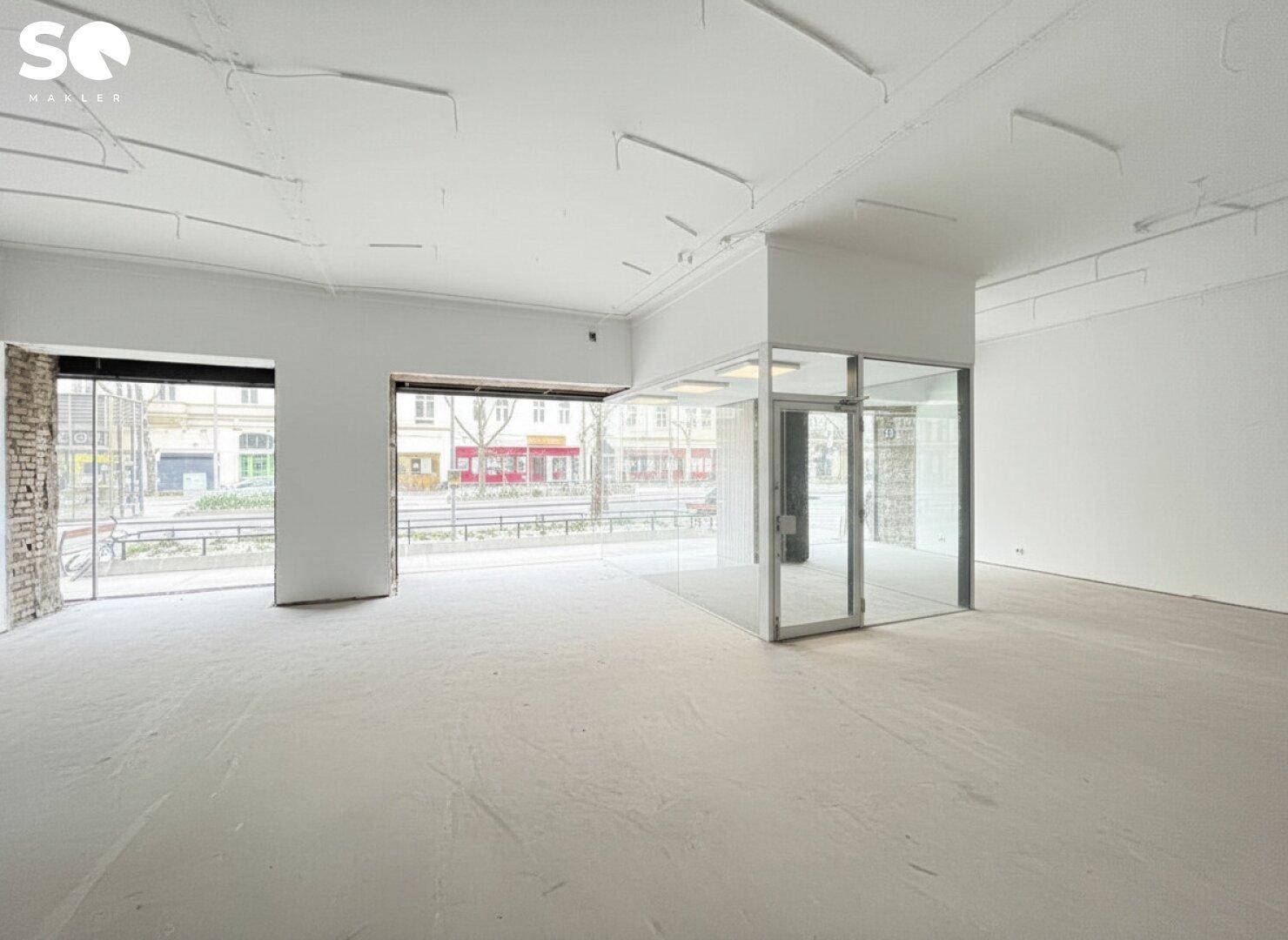 Renovierter Geschäftsraum mit hellen Wänden, modernem Boden und großer Fensterfront, die viel Licht hereinlässt.