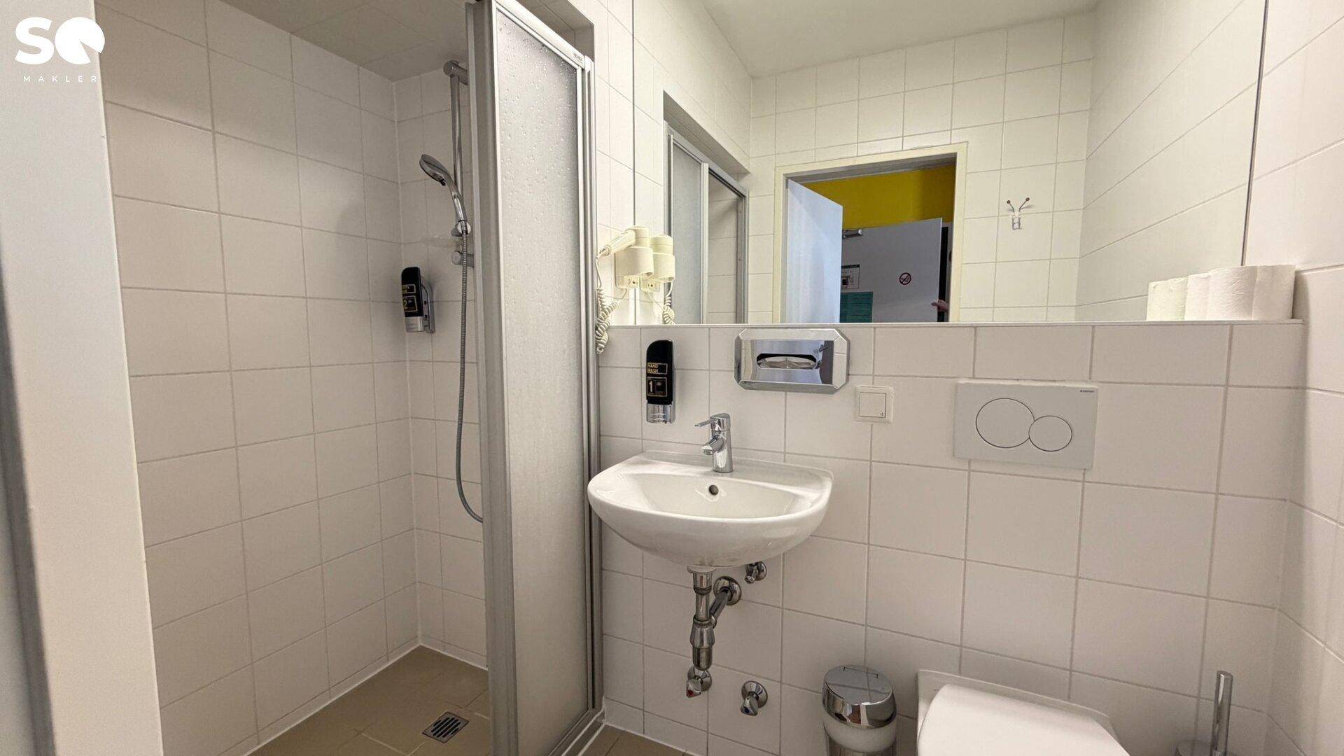 Helles Badezimmer mit weißen Fliesen, einer modernen Duschkabine und einem wandhängenden WC.