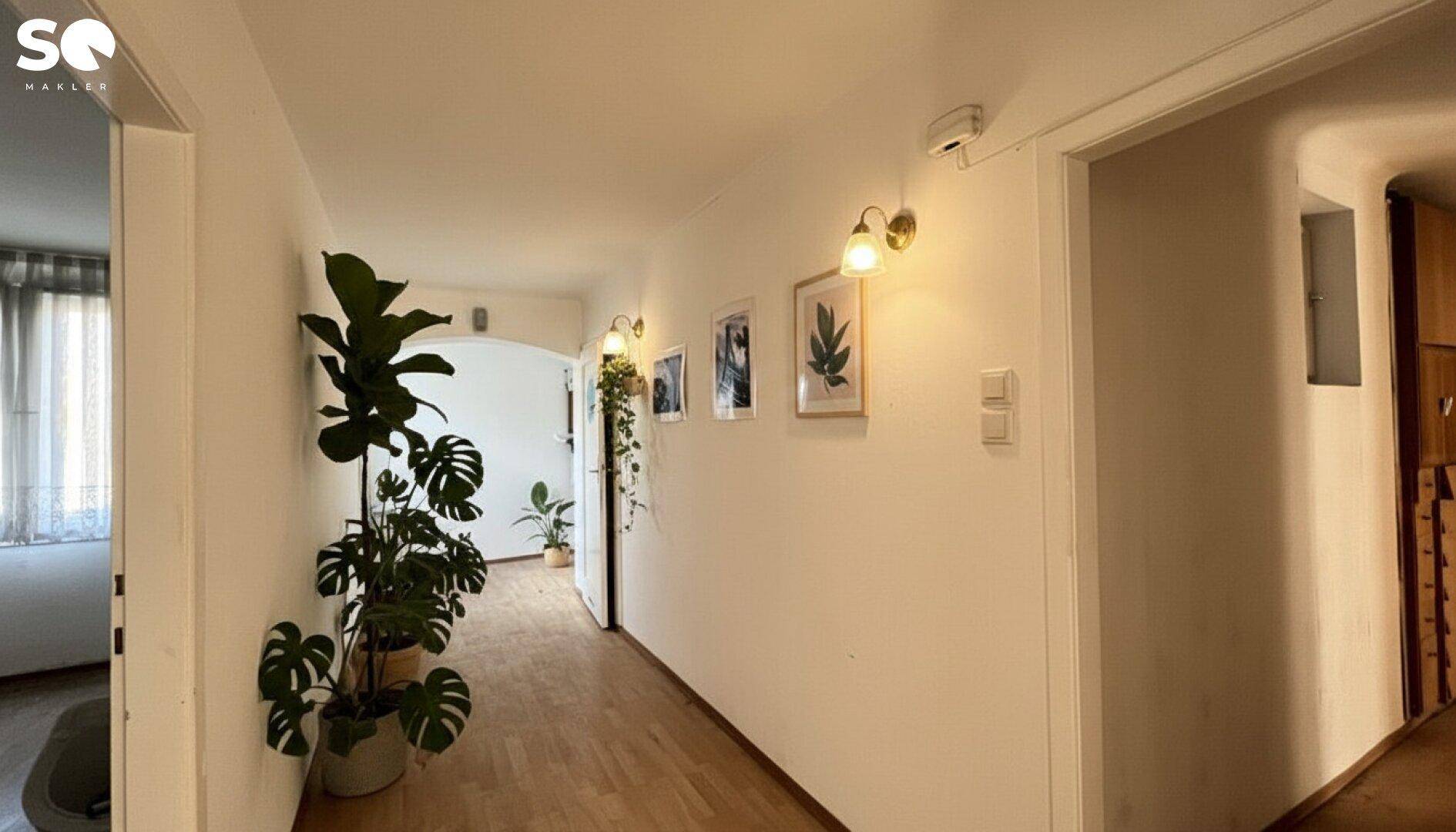 Heller Flur mit Pflanzen, Holzboden und dekorativen Bildern an der Wand.