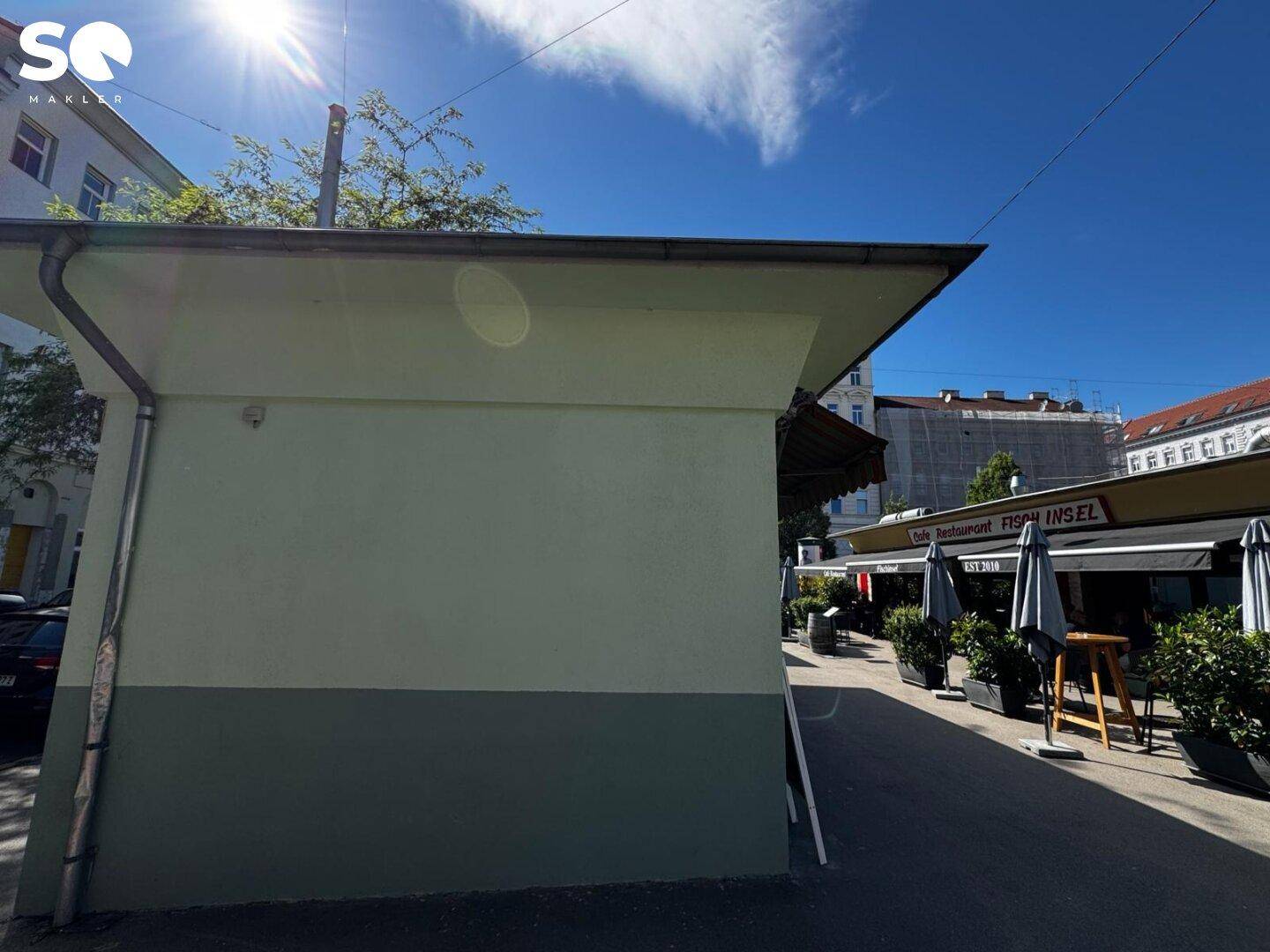 Seitenansicht eines kleinen Gebäudes mit zweifarbiger Fassade unter blauem Himmel an einem sonnigen Tag.