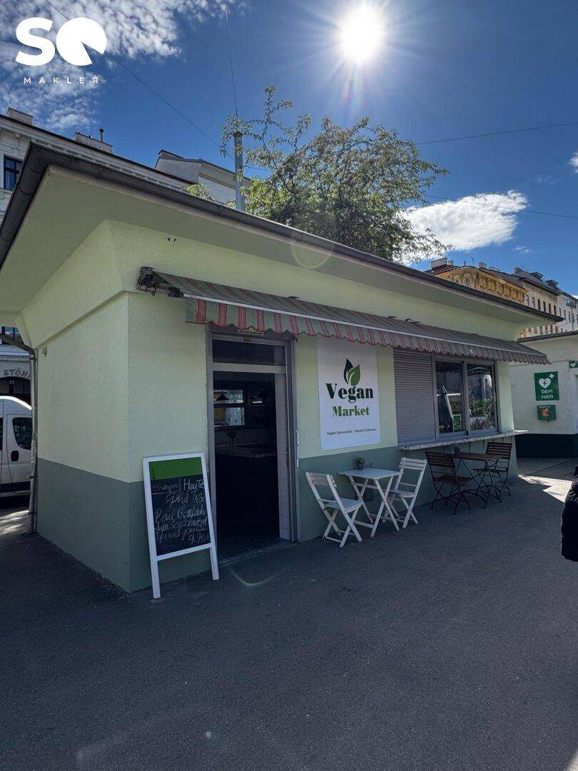 Frontansicht des "Vegan Market" mit Markise, Eingang und einladenden Außensitzplätzen auf dem Bürgersteig.